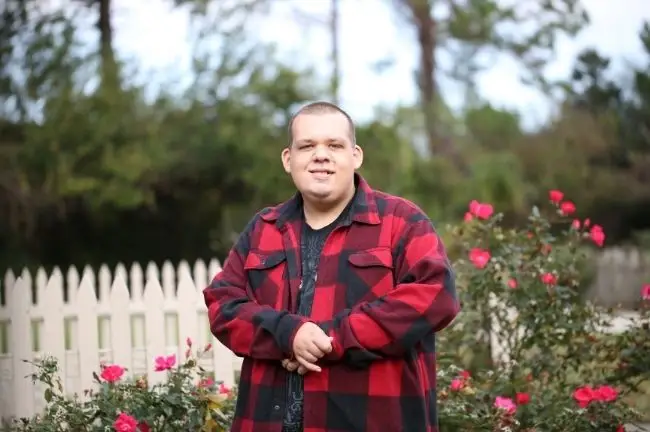A young man stands smiling in a garden of roses, representing independence supported by direct payments.