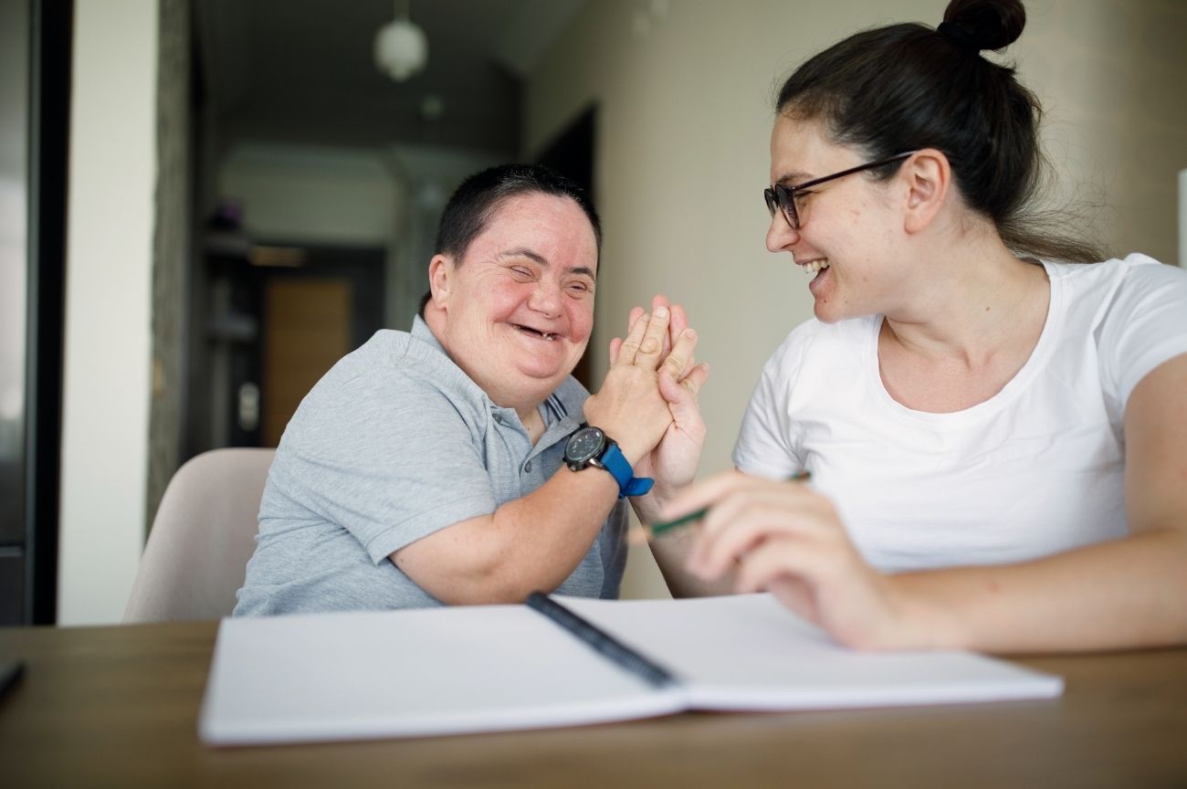 A man smiles as he is supported by his personal assistant.