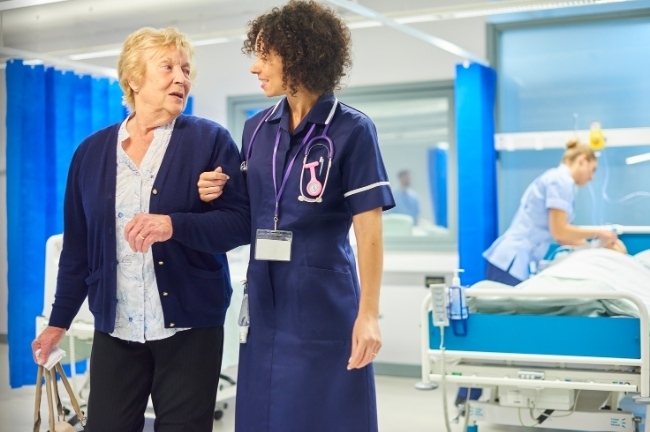 A nurse assists a woman out of the hospital as she prepares to start her reablement support with us.