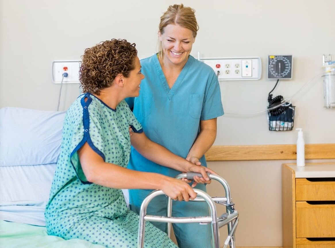 A woman in hospital focuses on standing with a frame while we prepare her home and reablement support for a smooth discharge.