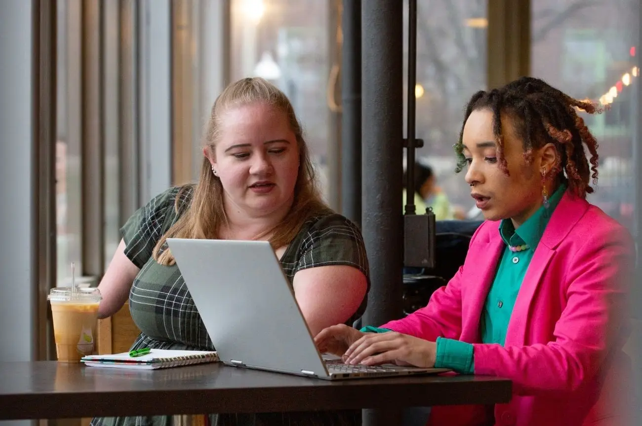 Two women focus on a laptop, discussing PA recruitment.