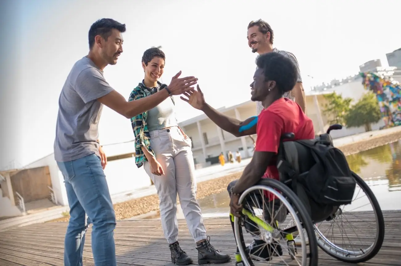 A man in a wheelchair smiles as he greets his friends, enjoying social and leisure time.