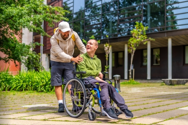A person in a wheelchair laughs with another person, representing respectful and person-centered support.
