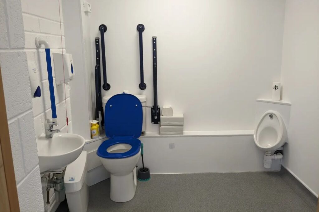 An accessible toilet with support rails on both sides and a red emergency pull cord beside the toilet.