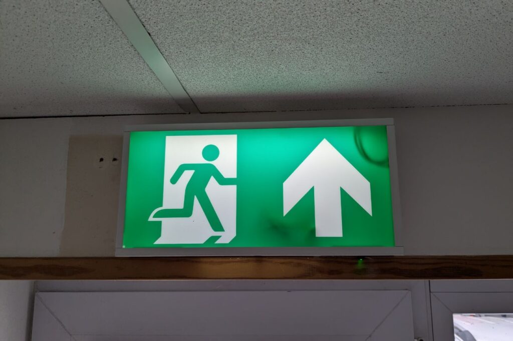 Green fire exit sign with a running figure and arrow, mounted above a doorway.