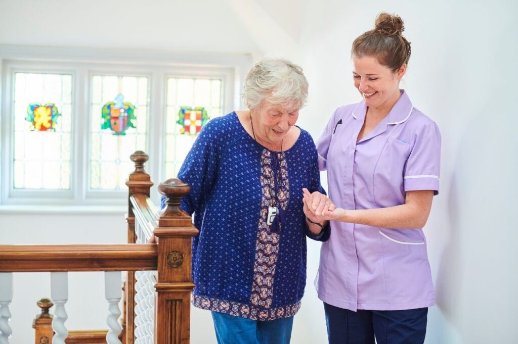Smiley support worker assisting an older lady up the stairs.